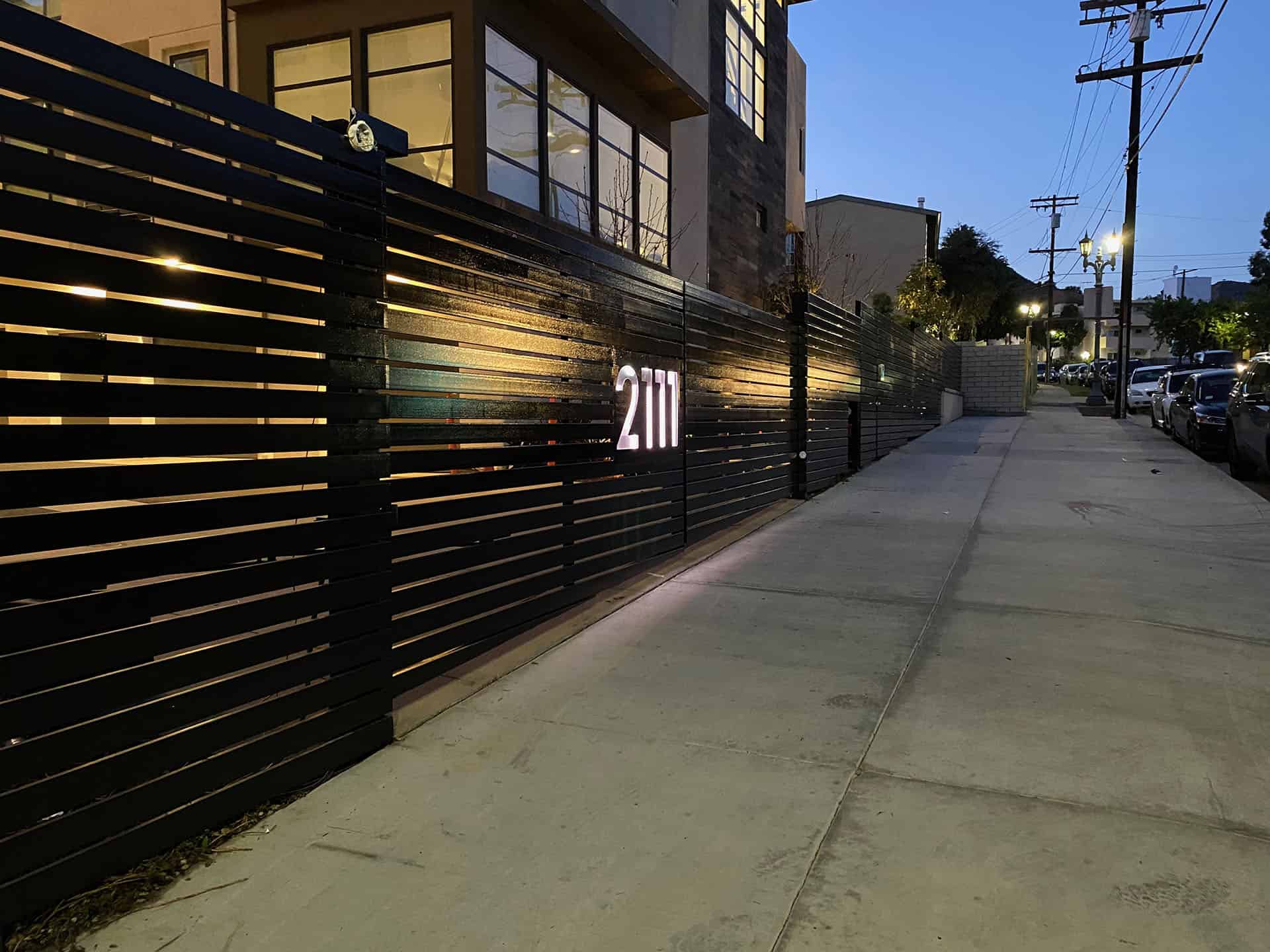 Black horizontal slat fence with illuminated house numbers